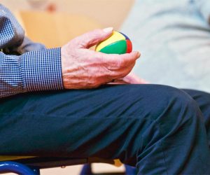Elderly man holding a colorful therapy ball indoors, promoting relaxation and health.